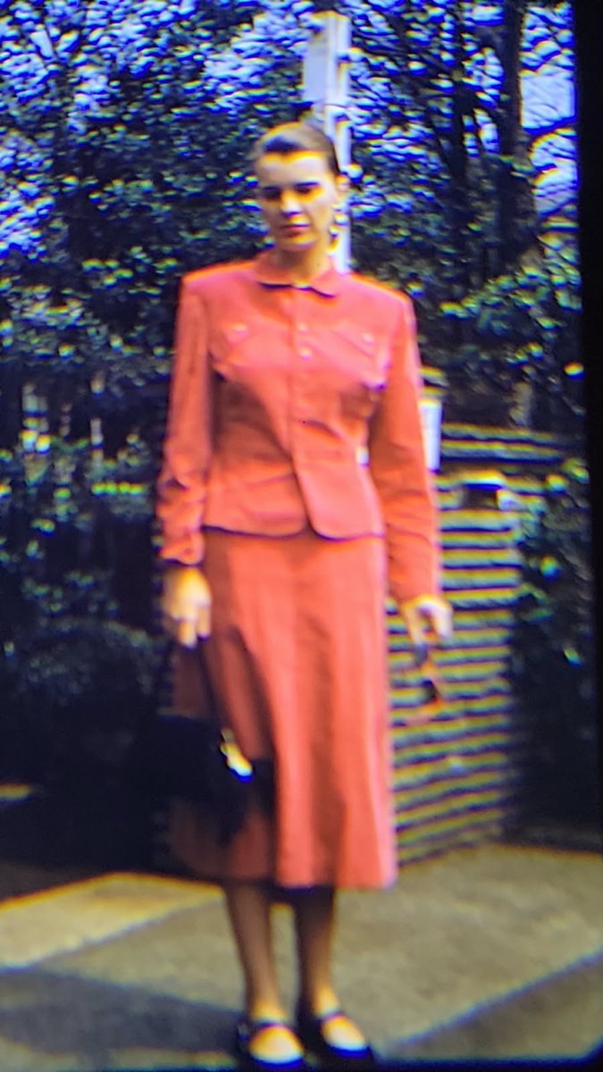 Joanne standing near a garden gate in a coral outfit